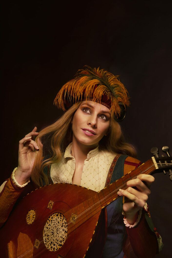 Photo de barde au cheveux long, avec un chapeau à plume et un instrument de musique en main