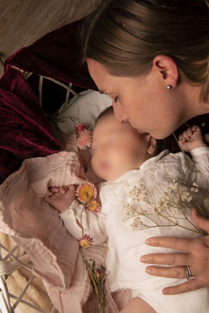 Photo bébé entouré de fleurs, une femme lui fait un bisous sur le front