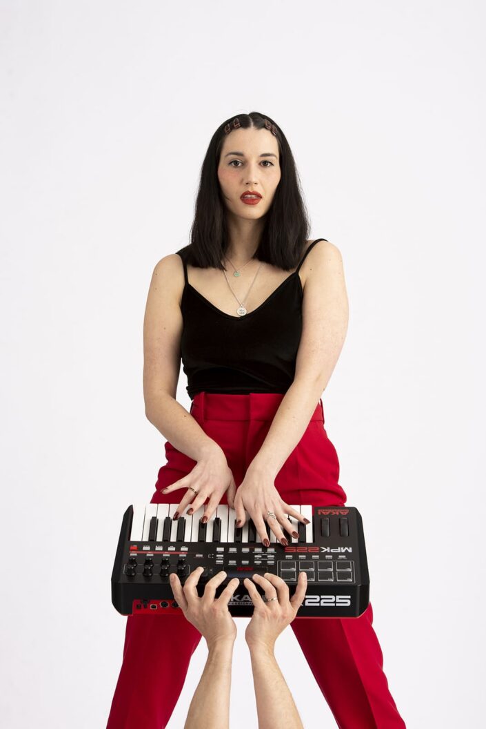 Photo femme avec un piano synthé. Elle porte un pantalon rouge et un haut noir.