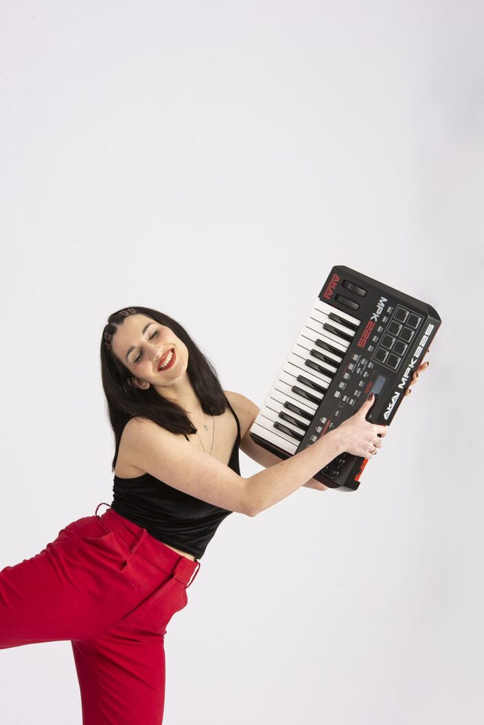 Photo femme avec un piano synthé. Elle porte un pantalon rouge et un haut noir.