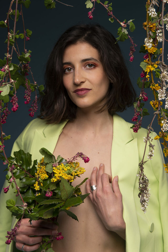 Photo portrait d'une femme avec une veste verte, la coupe au carré et qui est entouré de fleurs